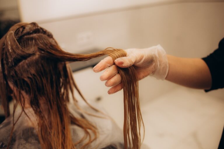 Une coiffeuse prépare une chevelure blonde avant d’appliquer une base châtain enrichie en pigments chauds