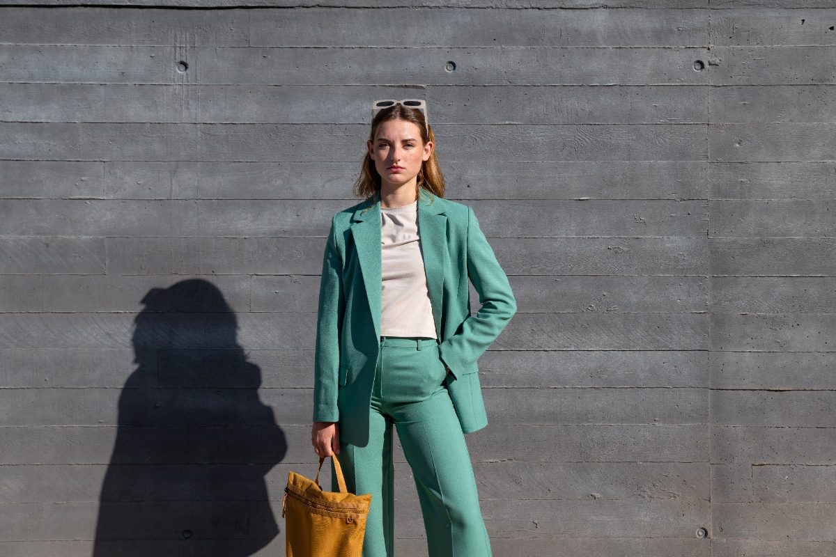 Blazer vert porté par une femme, avec un pantalon vert, une lunette et un sac marron