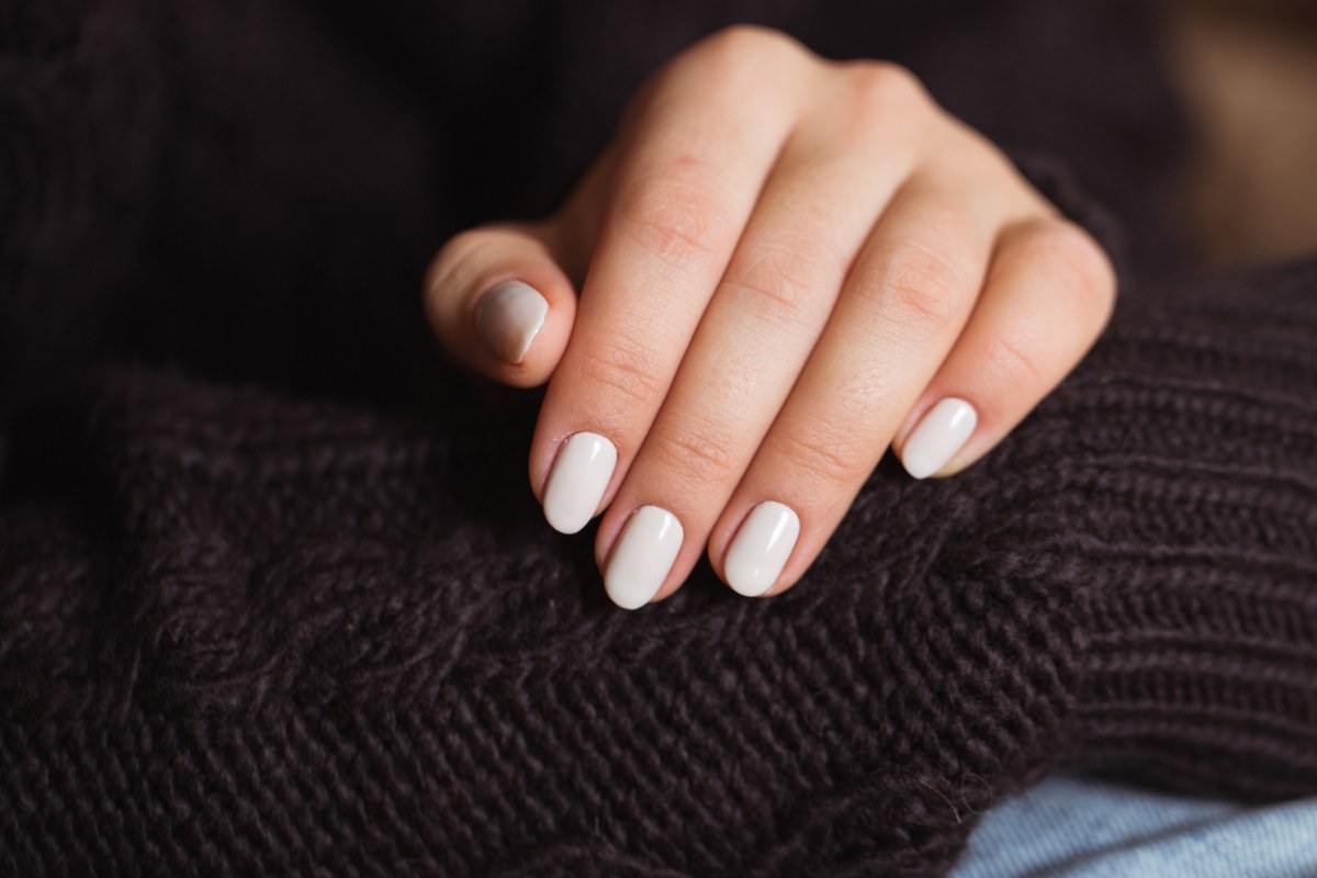 Une jolie main avec du vernis blanc laiteux