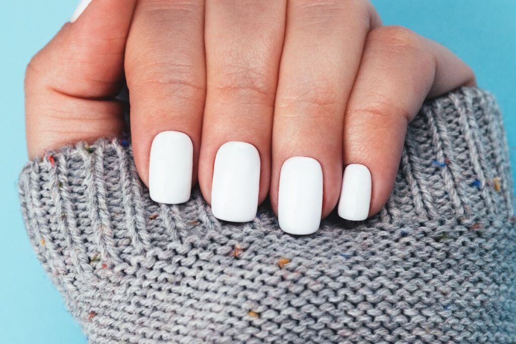 Main avec du vernis à ongle blanc laiteux