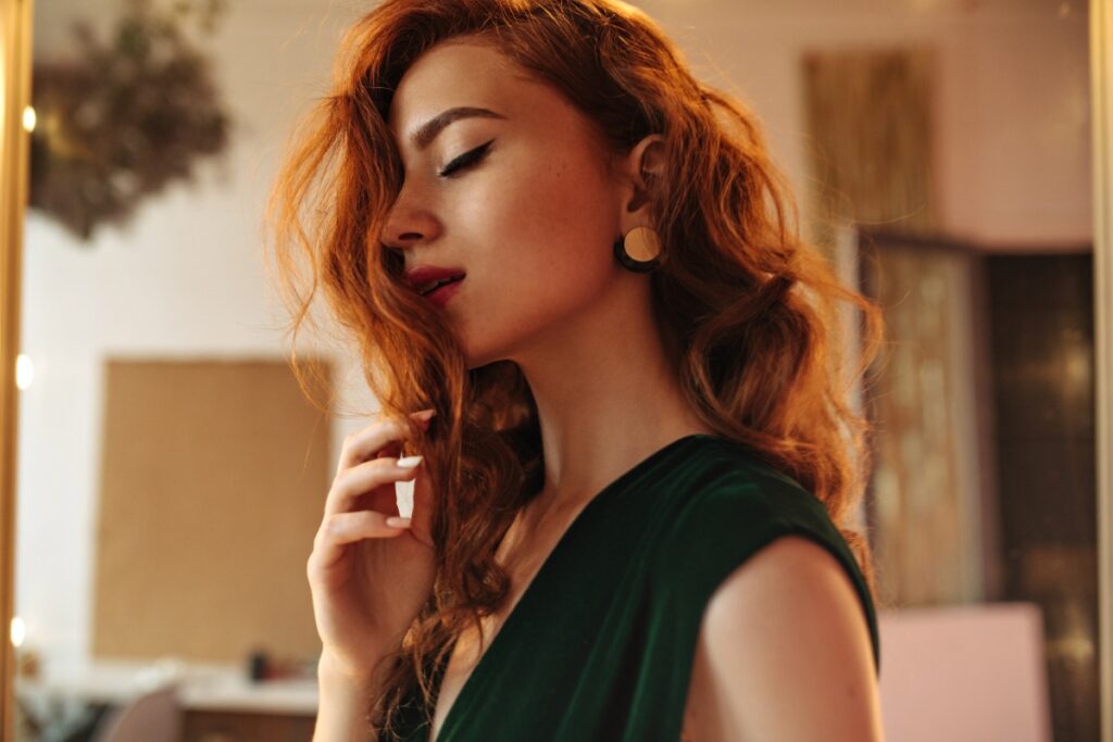 Une femme avec des cheveux roux ondulants, du maquillage et habillée en robe verte