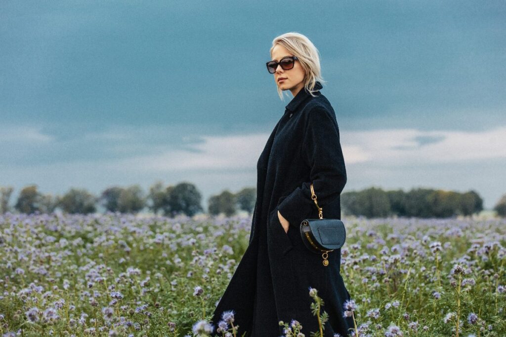 Une femme qio porte une robe noire avec un manteau et une lunette