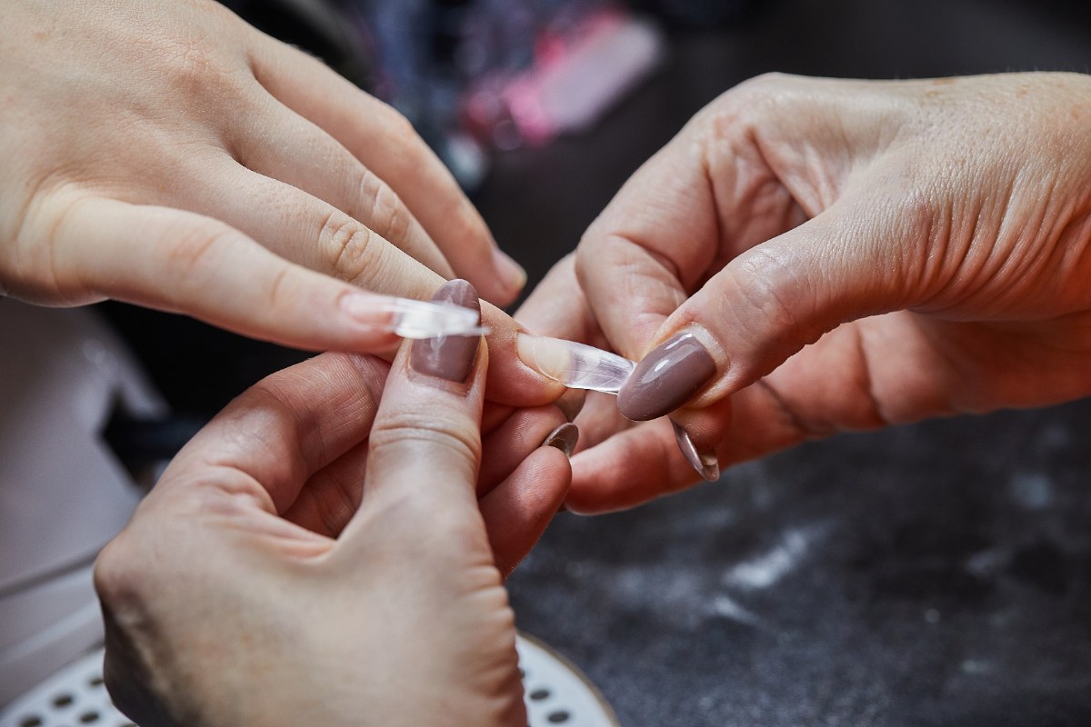 Une main qui applique une extension à ongle dans un salon