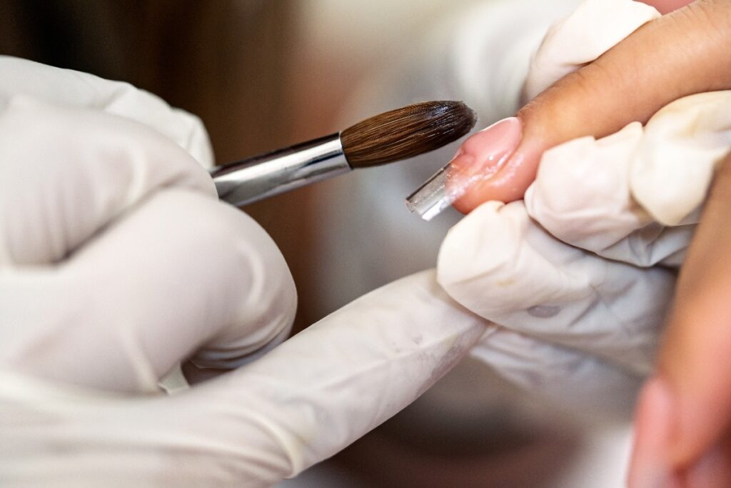 Un prothésiste ongulaire appliquant de l'acrylique sur l'ongle d'une personne