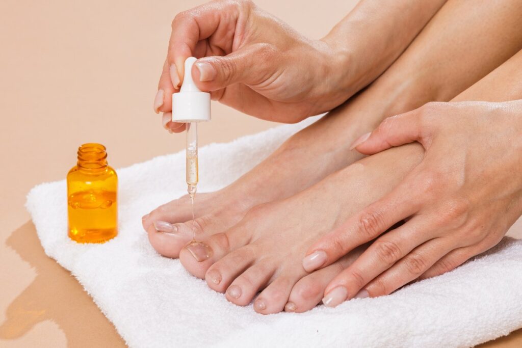 Une femme appliquant de l'huile essentielle sur les ongles du pieds